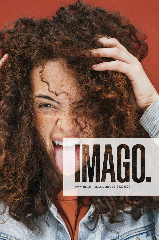 Young curly haired woman with hands in hair sticking out tongue model released Symbolfoto JCMF02098