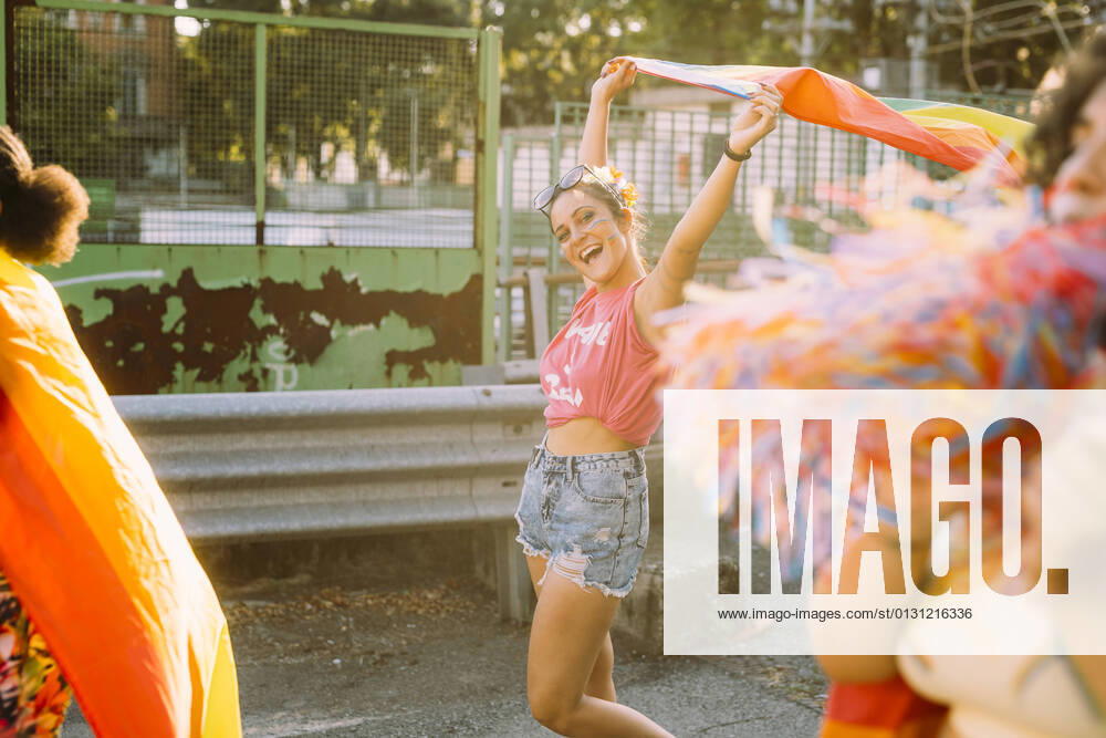 IMAGO Creative: Frauenmonat, Feministischer Aktivismus Cheerful female friends walking with rainbow flag on street model released Symbolfoto MEUF03709