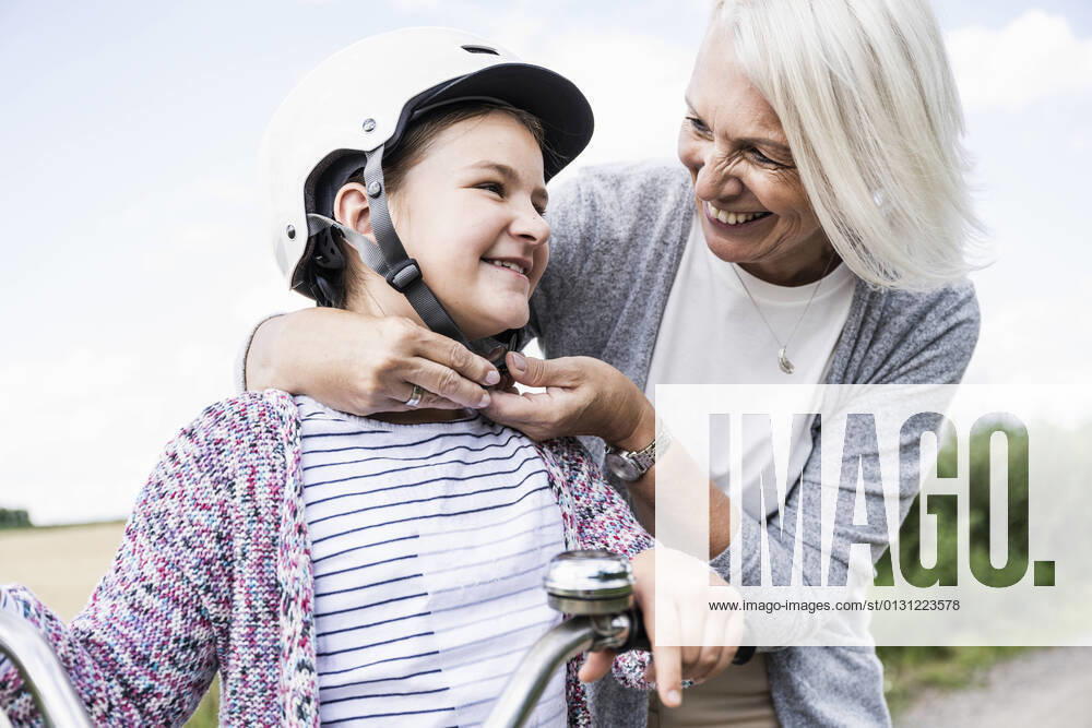 IMAGO Creative: Gesellschaft, Integration Smiling woman putting cycling helmet to girl while standing by bicycle model released Symbolfoto UUF24172