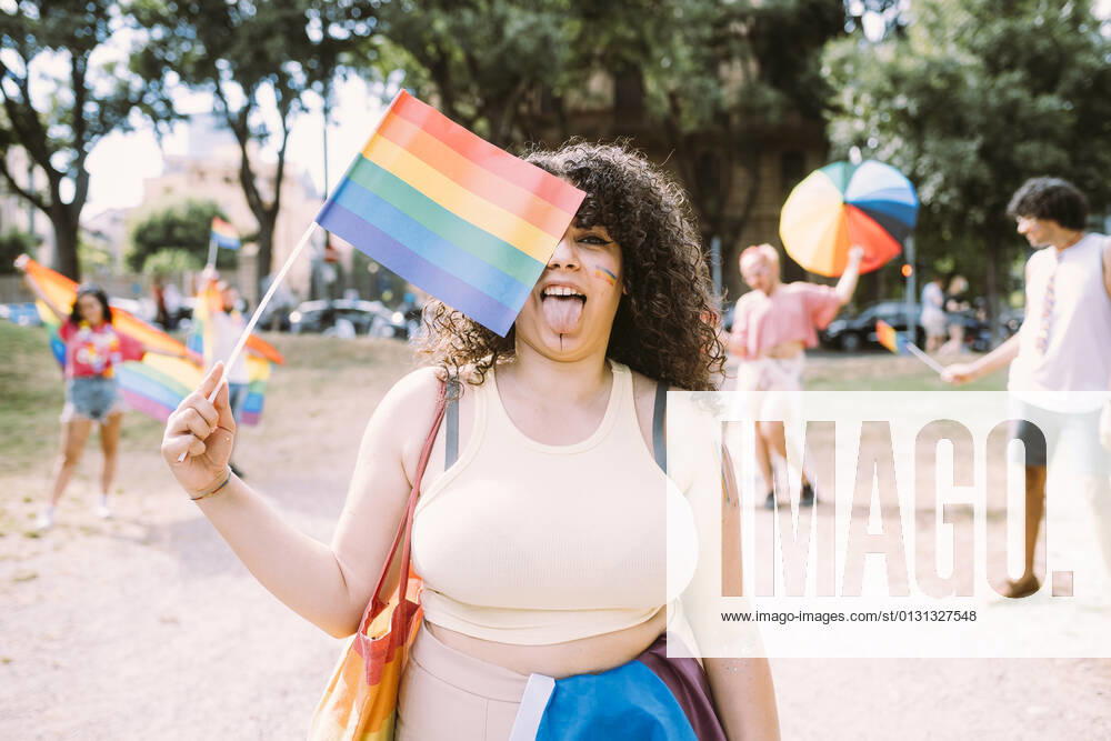 Young woman holding rainbow flag while friends in background at park model released Symbolfoto MEUF03621