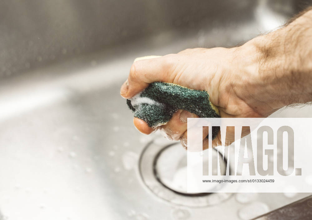 Man with sponge and detergent cleans sink under running water