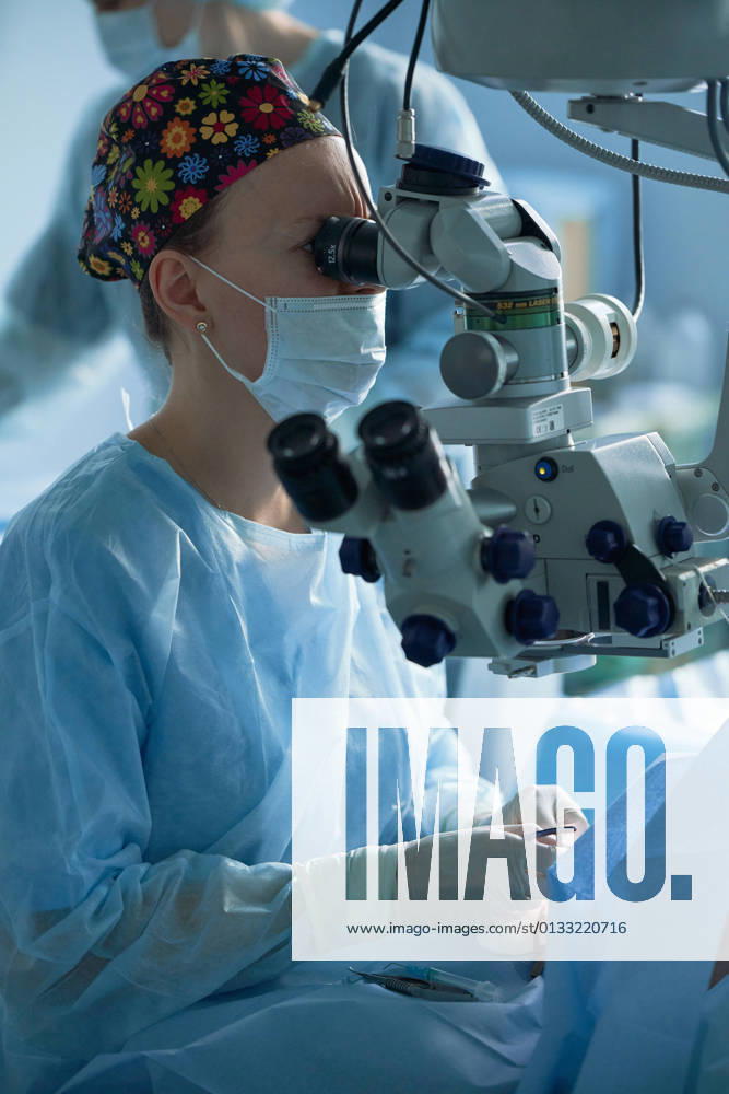 Adult female doctor in sterile mask and ornamental medical cap looking through surgical microscope against crop coworker in hospital, Model released SergeyMironov_Surgery_5.jpg