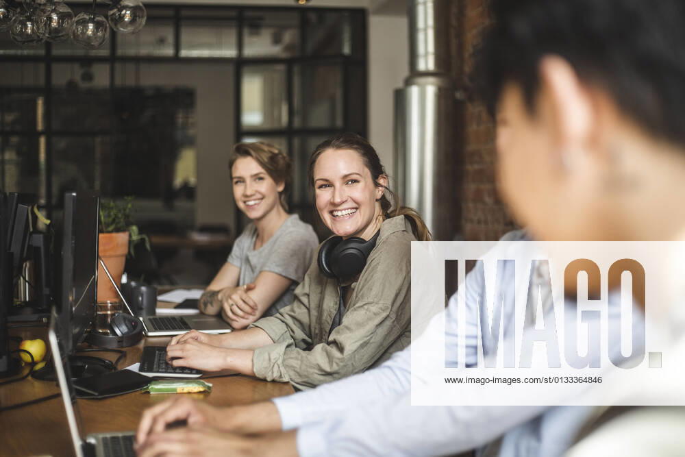 Happy male and female colleagues talking while working at startup company Sweden, Stockholm, model released, property released