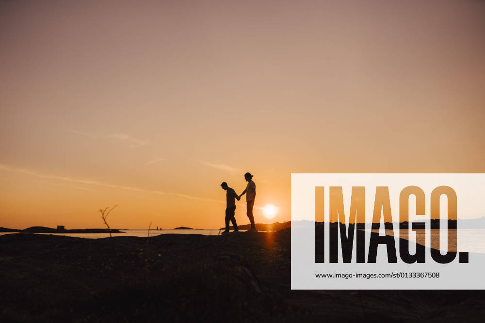 Male friends holding hands while walking at lakeshore during sunset Sweden, Gothenburg, model released