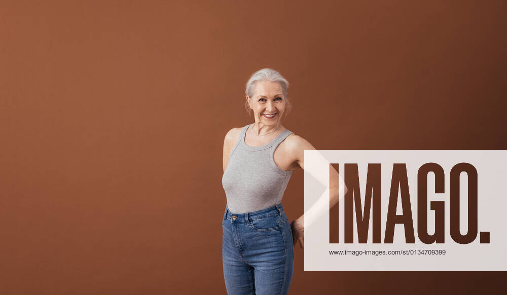 IMAGO Creative: Internationaler Frauenmonat, Gesundheit, Frauen in der Menopause Portrait of a mature woman in casuals standing at brown background in studio Portrait of a mature woman in casuals standing at brown background in studio