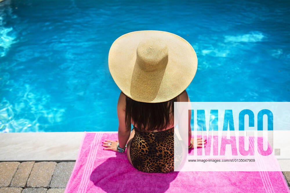 Rear view of young woman in sunhat sitting at poolside, 28.08.2014,