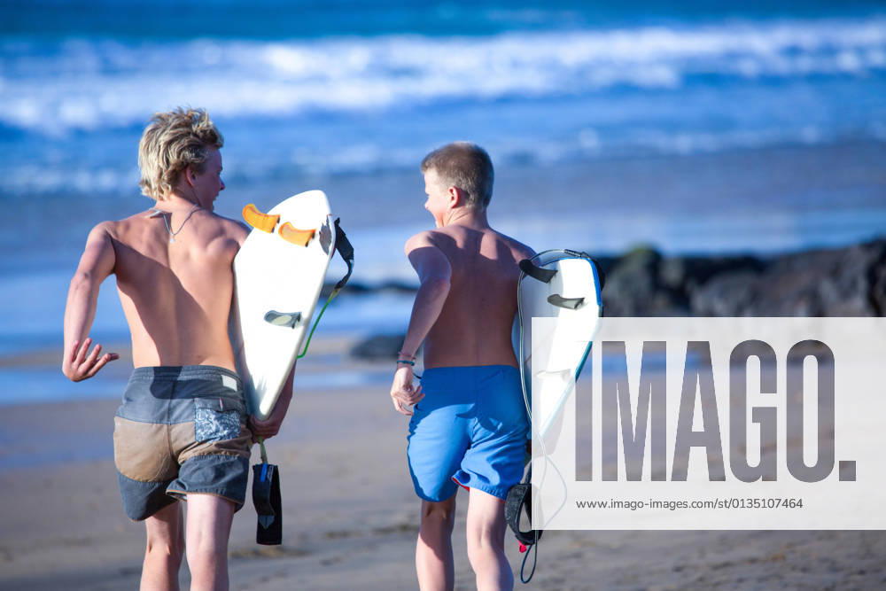 IMAGO Creative, Jahreszeit Sommer, Sommerferien Two teenage male surfers running toward sea, Fuerteventura, Spain, 29.04.2015,