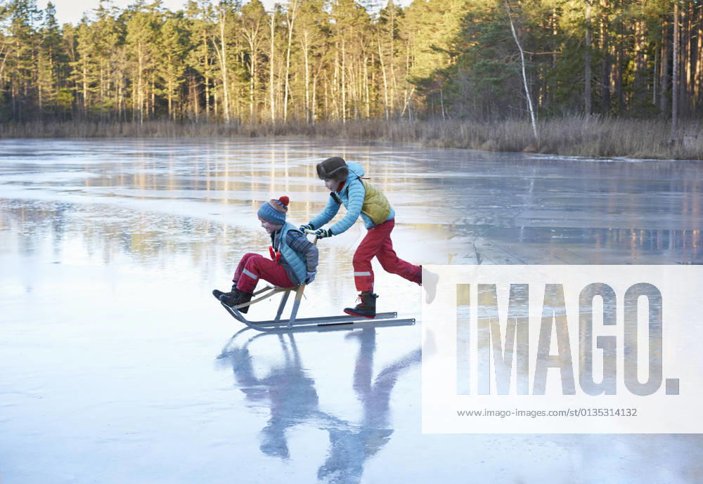 Boy pushing his brother on sleigh across frozen lake, 02.07.2018,