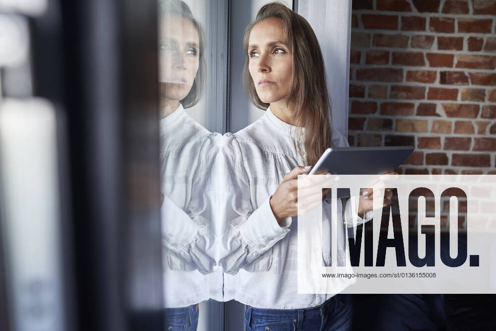 Businesswoman with digital tablet looking through window at home model released Symbolfoto property released ABIF01468