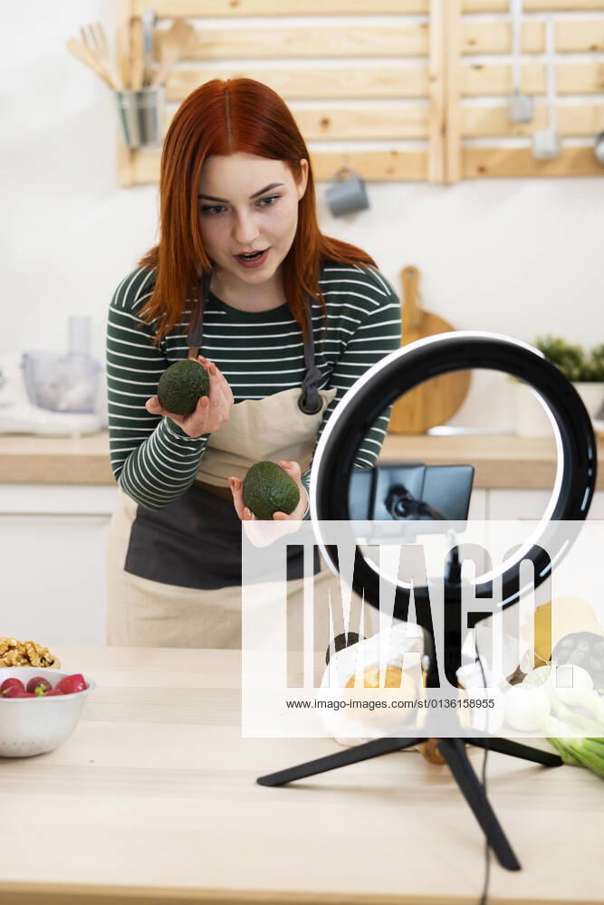 Woman filming through mobile phone while standing in kitchen model released Symbolfoto property released GIOF13210