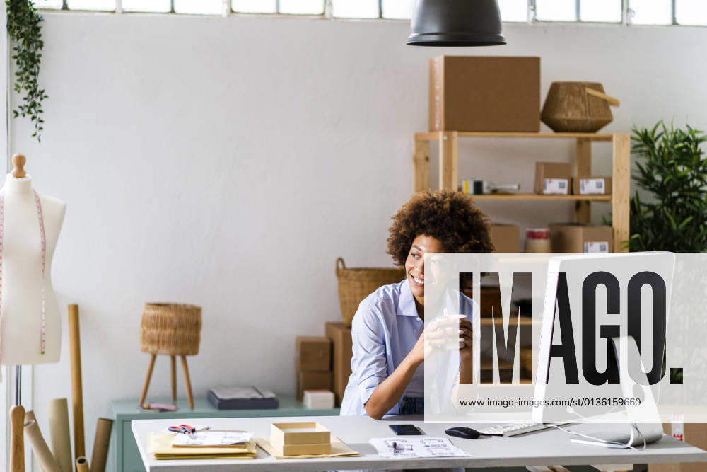 Smiling female design professional holding mug while sitting at desk in studio model released Symbolfoto property released GIOF13479