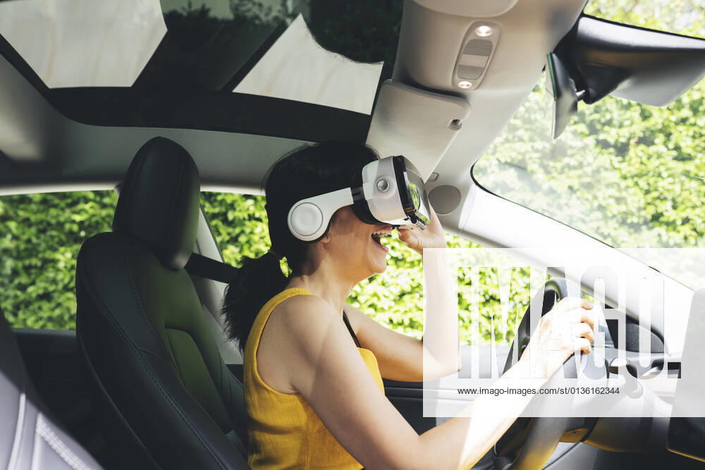 Excited woman wearing virtual reality simulator while driving electric car model released Symbolfoto JCCMF03738