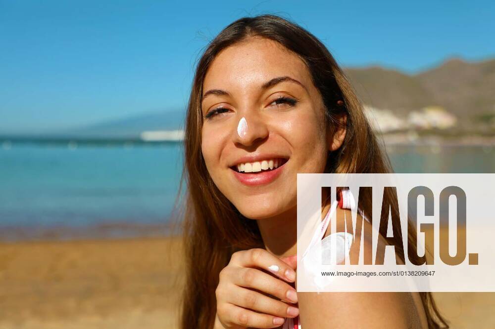 IMAGO Creative, Jahreszeit Sommer, Sonnenschutz Beautiful happy cute woman applying suntan cream to her nose and shoulder with beach background model released, Symbolfoto, 13.10.2020,