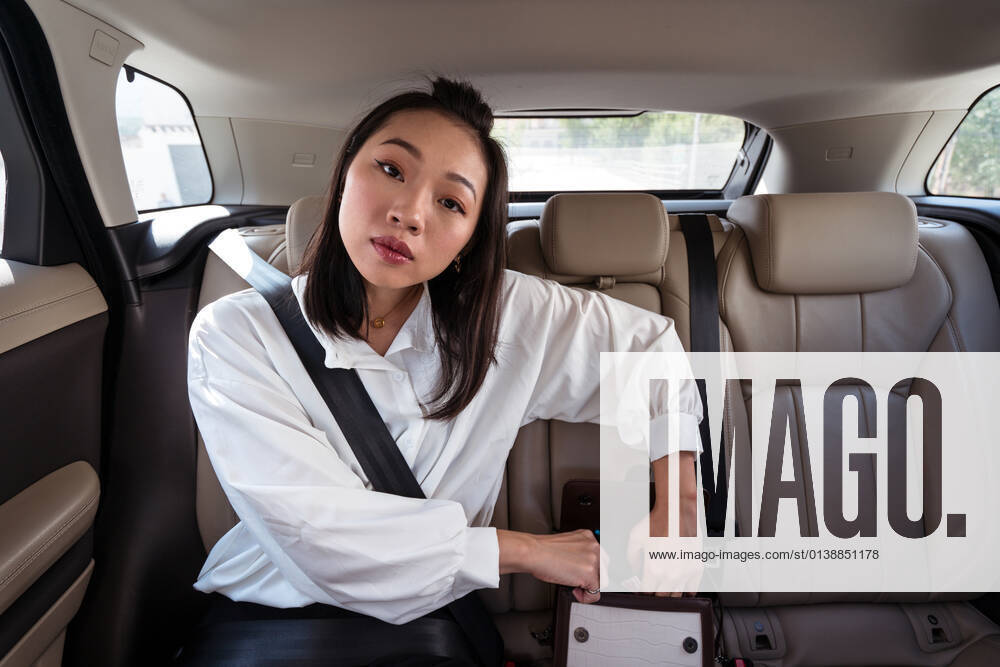 Young ethnic female with fastened seat belt opening bag on backseat of car and looking at camera with interest, Model released JuanAlbertoRuiz_Uber_7.jpg