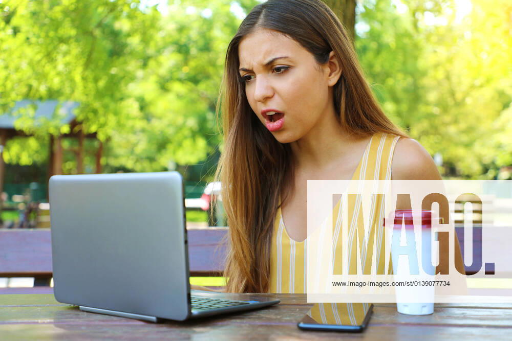 Disappointed business woman sitting in the park looks at the laptop raging after working hard all the morning.