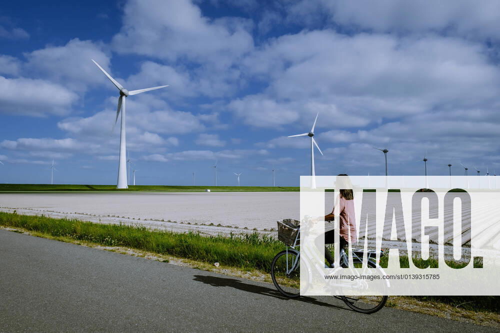 IMAGO Creative: Nächste Generation, Sozial- und klimabewusst young woman electric green bike bicycle by windmill farm , windmills isolated on a beautiful bright day Netherlands Flevoland Noordoostpolder young woman electric green bike bicycle by windmill farm, windmills isolated on a beautiful bright day Netherlands Flevoland Noordoostpolder Holland