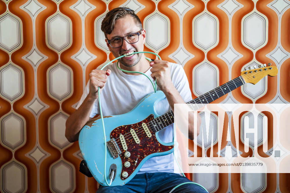 Young male guitarist biting guitar cable in front of wall model released Symbolfoto property released DLTSF02242