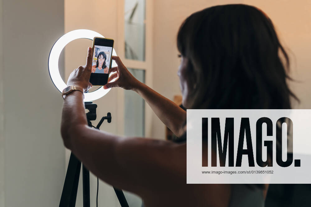IMAGO Creative: Clickbait, Sport und Fitness Mature female influencer adjusting smart phone on ring light at home model released Symbolfoto property released JRVF01875