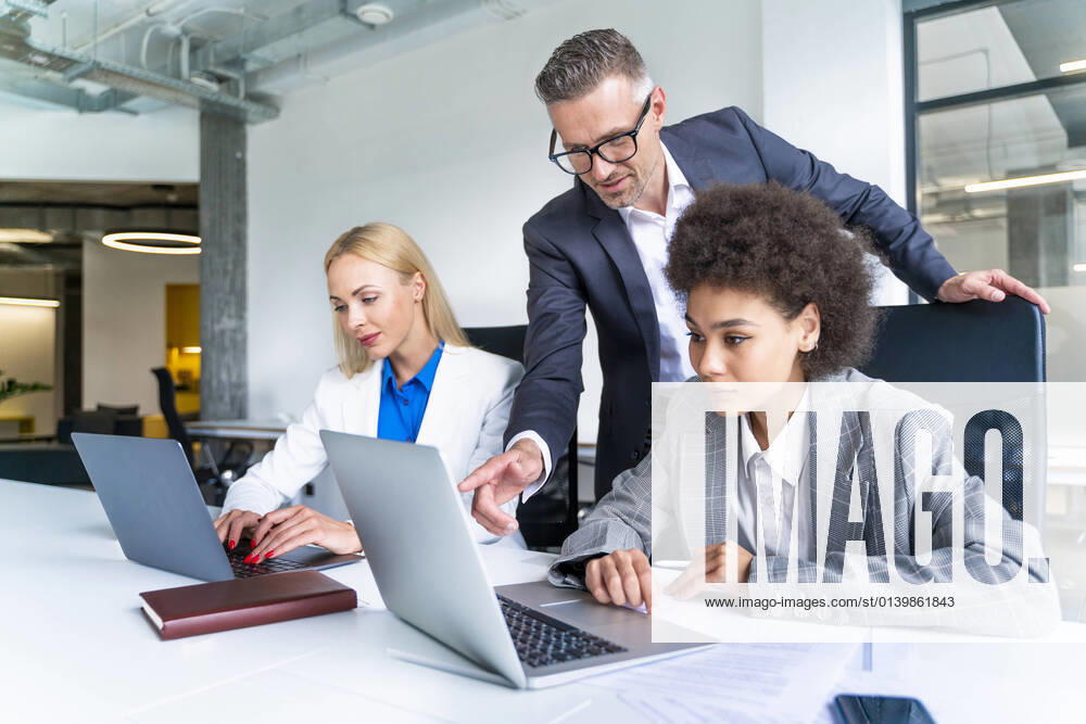 Male business professional explaining female colleague over laptop at desk model released Symbolfoto property released OIPF01191