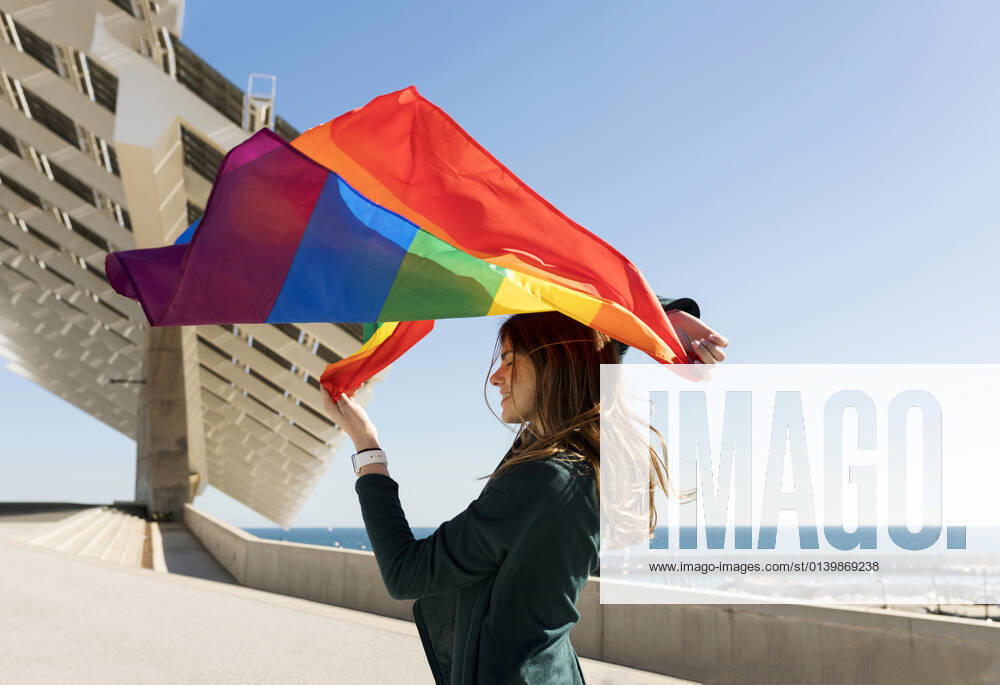 Woman holding rainbow flag near solar energy panel during sunny day model released Symbolfoto VABF04362