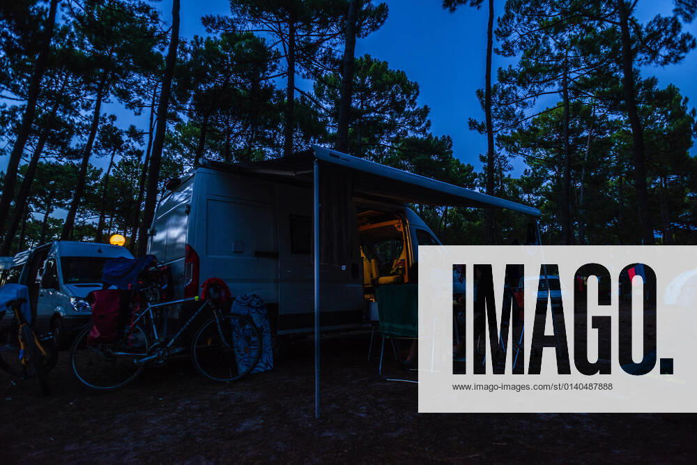 Campers sitting on camping chairs in front of their camper at blue hour on a warm summer evening at a campsite Bordeaux Gironde , Nouvelle Aquitaine, France Travelling with a campervan