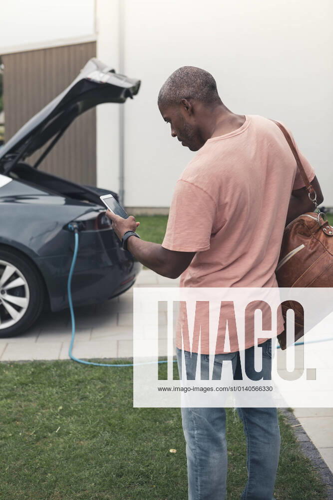 IMAGO Creative: Business, Innovative Technologie-Lösungen Rear view of man using smart phone while standing with backpack at charging station Sweden, Skane, model released, property released