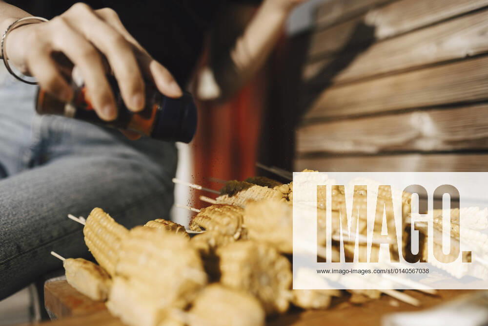 IMAGO Creative: Landleben - Essen Midsection of woman sprinkling pepper on sweetcorn while preparing food at party Sweden, Gothenburg, model released, property released