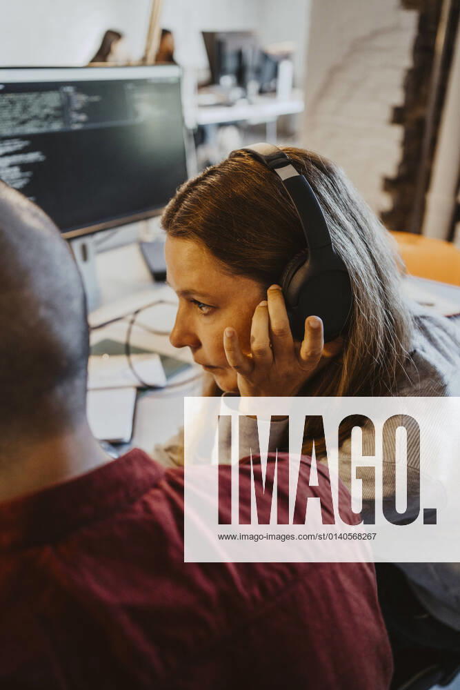 Female programmer listening through headphone while doing coding at startup company Germany, Berlin, model released, property released