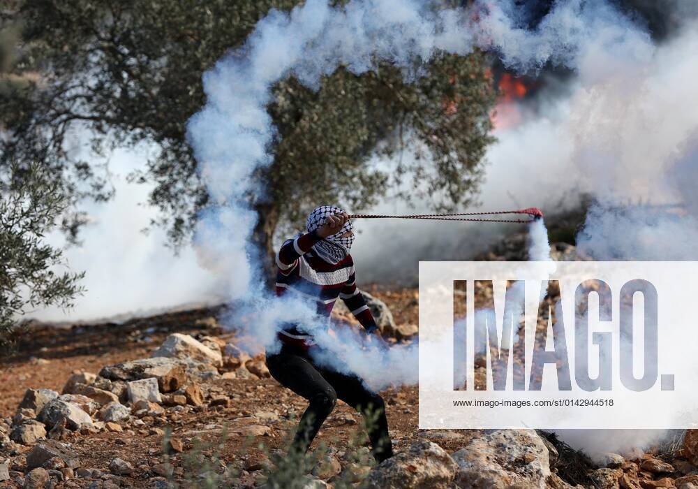 (211126) -- NABLUS, Nov. 26, 2021 -- A protester uses a slingshot to throw back a tear gas canister fired by Israeli soldiers in a protest against the expansion of Jewish settlements in the village of Beita, south of the West Bank city of Nablus, Nov. 26, 2021. (Photo by Ayman Nobani Xinhua) MIDEAST-NABLUS-CLASHES ChenxLin