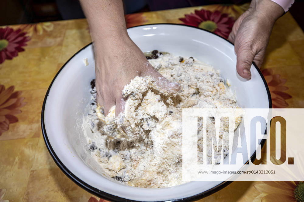 Mix and knead the ingredients for stollen dough with your hands in a white bowl 1049002938