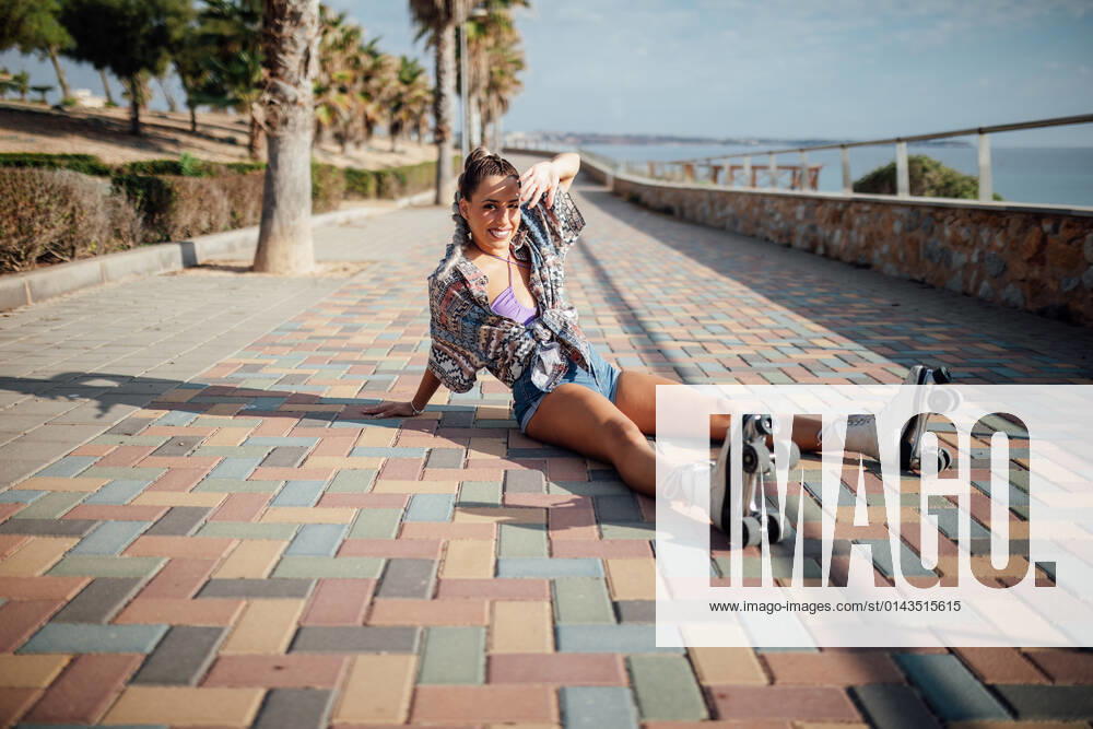 IMAGO Creative, Jahreszeit Sommer, Sommer in der Stadt Full body side view of sportive female in roller skates sitting on colorful paved pathway on street with tall trees DaniNavarro_RollerSkaterYoungWoman_4.jpg