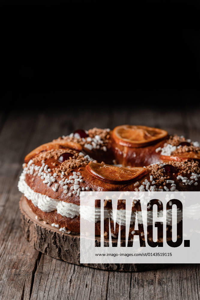 King s cake with cream and sprinkles decorated with orange slices and cherries and placed on wooden table PimientaDulce_RosconOfKings_3.jpg