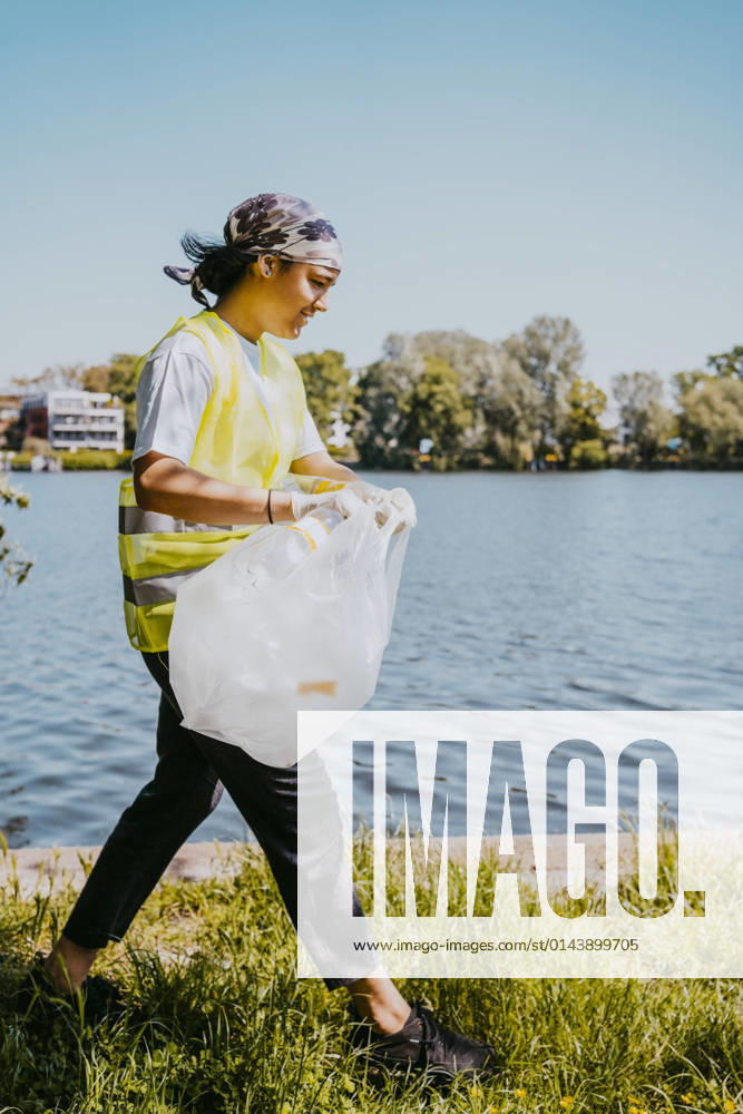 IMAGO Creative: Nächste Generation, Sozial- und klimabewusst Female environmentalist walking with plastic bag by lake Germany, Berlin, model released