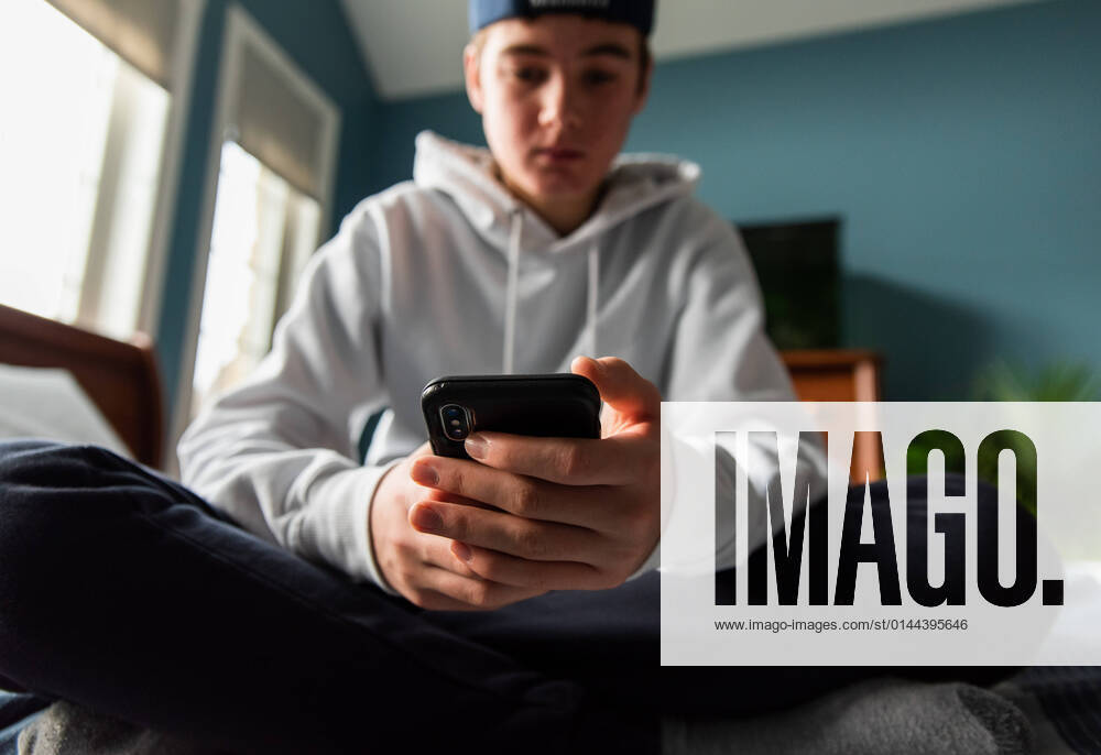 IMAGO Creative: Gesellschaft, Armut Low angle of teen boy in white sweater on smartphone in bedroom. Kingston, Ontario, Canada CR_DOHO211209E-877793-01 ,model released, Symbolfoto
