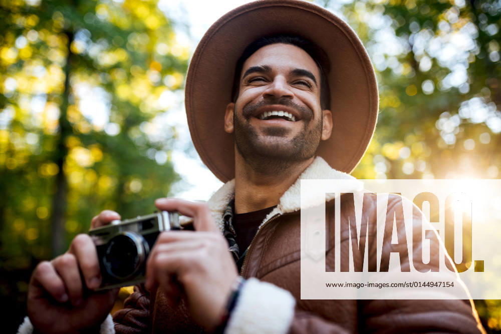 Cheerful male photographer in stylish wear with vintage camera of nature while standing on asphalt path near tall green trees during trip, Model released SergioVictorVega_MaikyPaola_21.jpg