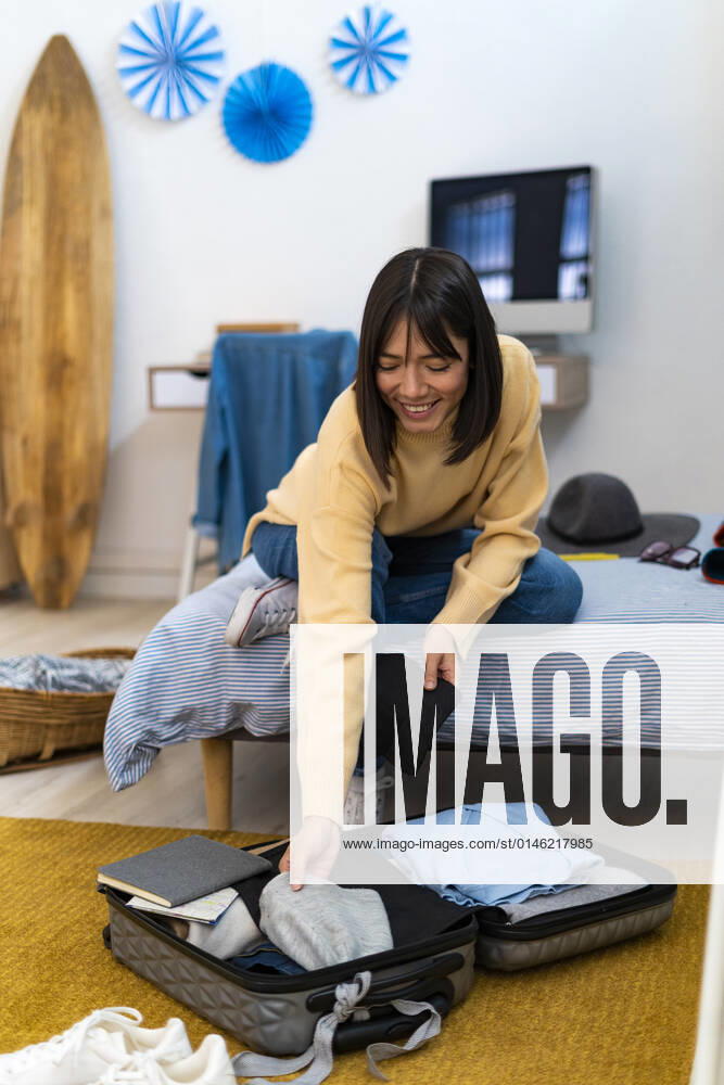 Smiling woman packing bag in bedroom at home model released property released, GIOF14221