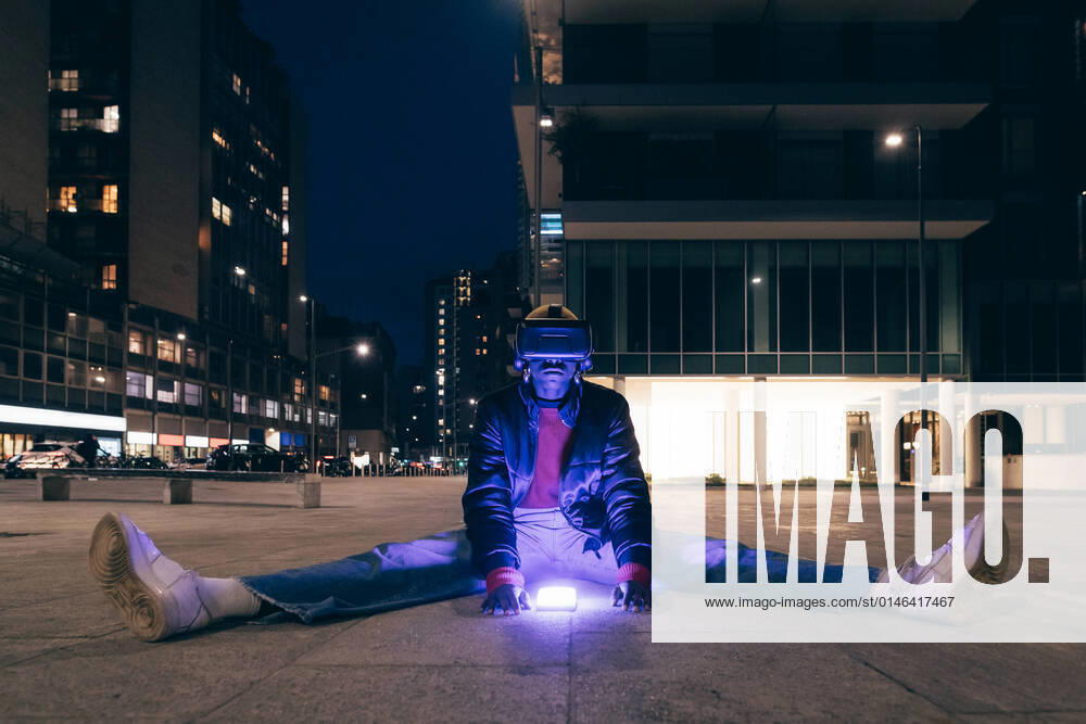 IMAGO Creative: 2022 Aussichten Italy, Woman withÃäVR goggles sitting on sidewalk in city at night Italy, Woman withÃäVR goggles sitting on sidewalk in city at night