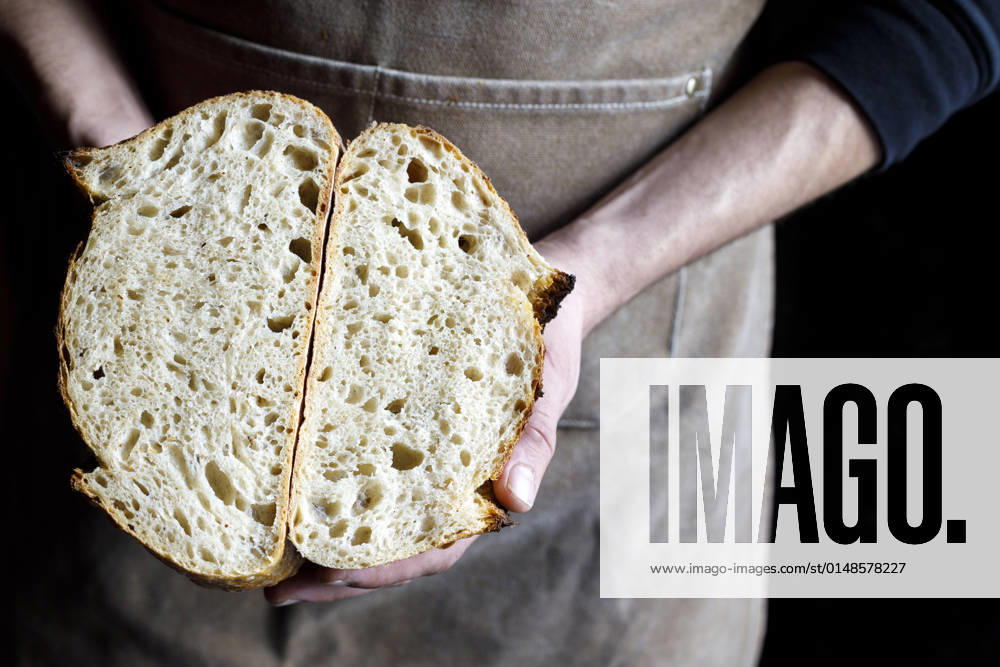 Baker holding halved loaf of bread at bakery model released property released, IFRF01296