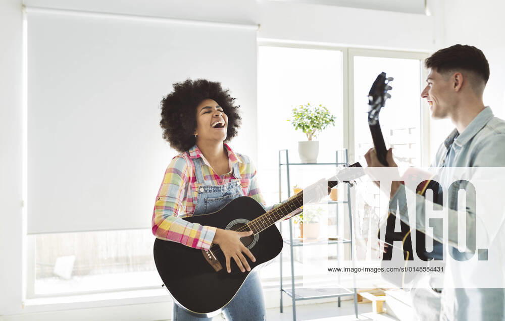 IMAGO Creative: Bildung, Musikerziehung Cheerful young couple playing guitar together at home model released property released, JCCMF05034