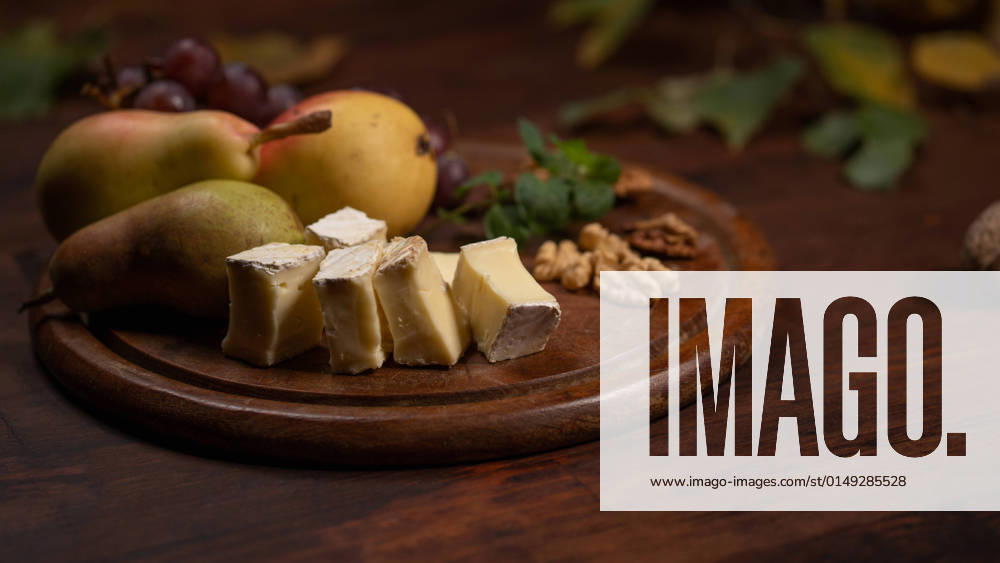 Snacks set: cheese, grapes, pear and three walnuts on a wooden table. Brie cheese with fruits, grapes, walnuts on a dark wooden plate and wooden board Snacks set: cheese, grapes, pear and three walnuts on a wooden table. Brie cheese with fruits, grapes, walnuts on a dark wooden plate and wooden board.