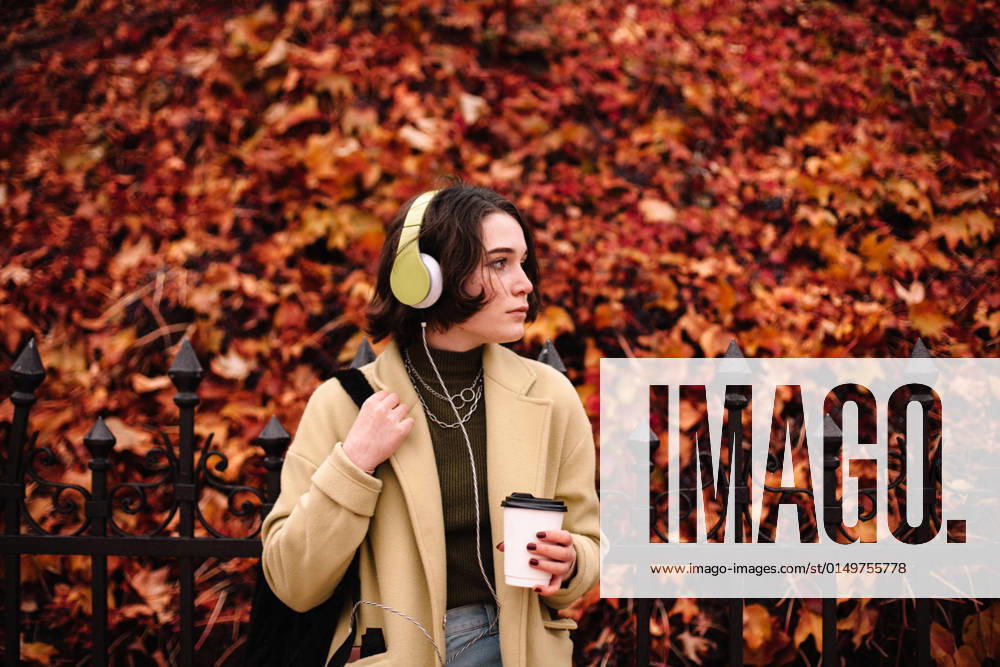 IMAGO Creative, Jahreszeit Herbst, Ferien IMAGO Creative: Ende des Sommers Young woman listening music in headphones standing in city in autumn CR_DMBE220203-885866-01 ,model released, Symbolfoto