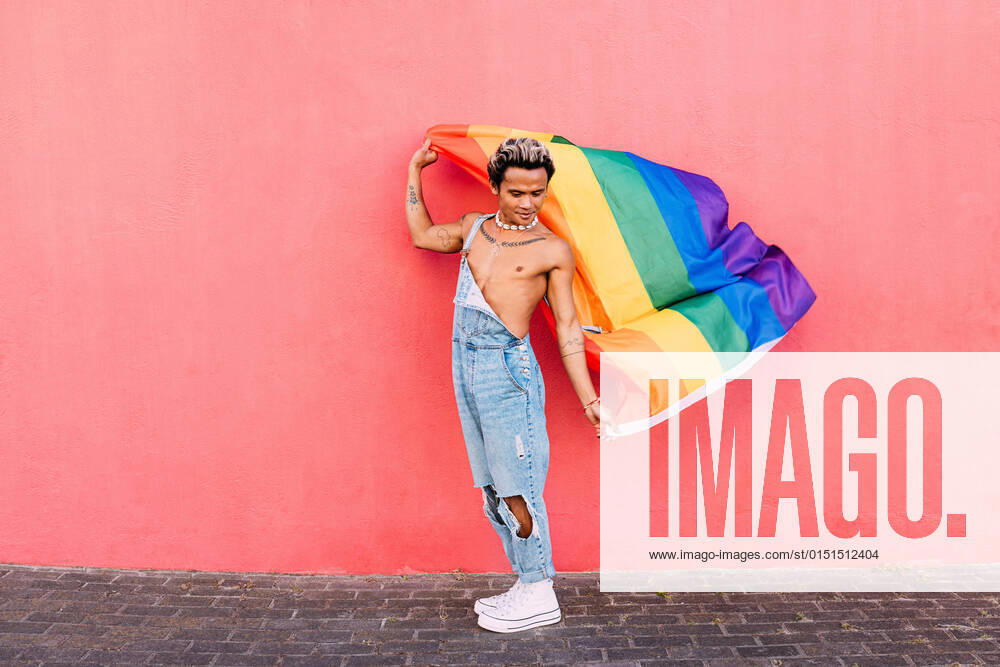 IMAGO Creative: Pride Month, Juni 2022 Gay male holding a rainbow LGBT flag in city against pink wall