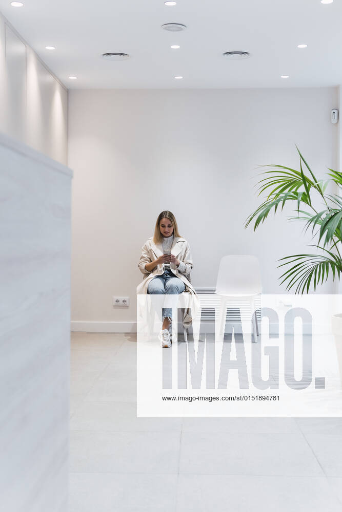 Woman using smart phone sitting in waiting room at clinic model released property released, PNAF03062