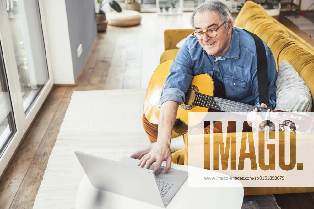 Senior man with guitar watching online tutorial on laptop in living room model released property released, UUF25348