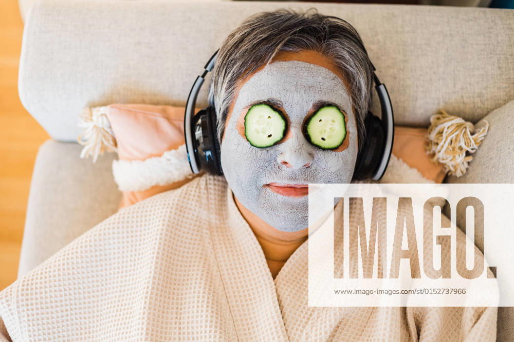 Top view of female with anti aging clay mask on face and cucumbers on eyes listening to music while lying on couch, Model released AlbaCaro_SkinCare_68.jpg