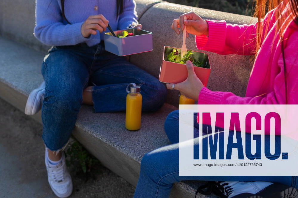 IMAGO Creative, Jahreszeit Sommer, Sommer in der Stadt Side view of anonymous cheerful Hispanic female friends eating salad while sitting on stone bench with water bottles on sunny street DavidMunoz_JenniferAndAlejandraLifestyle_2.jpg
