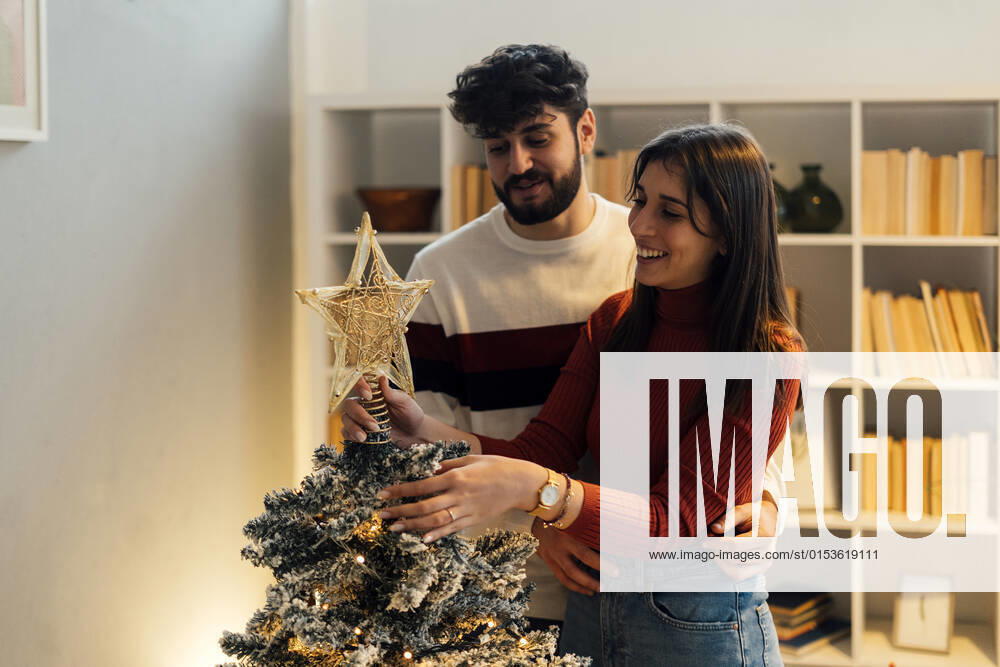 Happy couple decorating and putting star on Christmas tree at home model released property released, GIOF14896