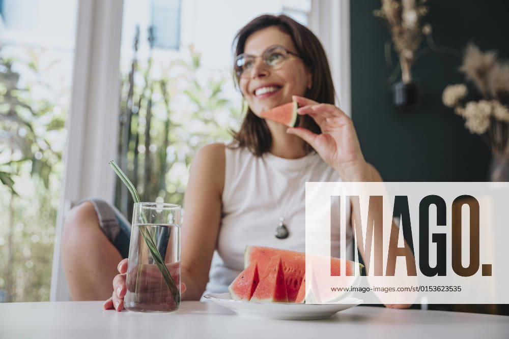 Woman sitting at home holding drinking glass by watermelon slice on table model released property released, MFF08845