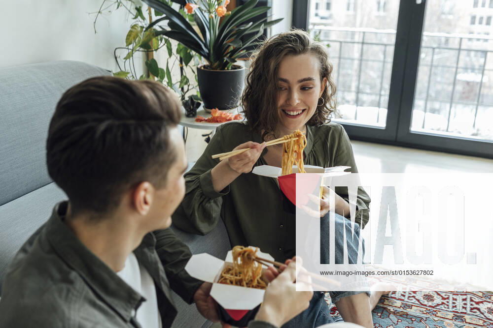 Happy woman and man with take out food talking in living room at home model released property released, VPIF05382