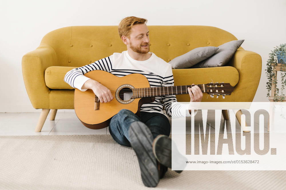 Young man playing guitar sitting in front of sofa at home model released property released, XLGF02886